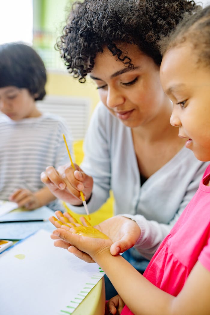 Home Teacher assists children with painting in a vibrant, creative classroom setting.